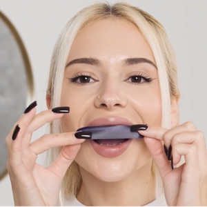 Mujer colocándose una tira blanqueadora morada modosmile sobre los dientes superiores frente al espejo