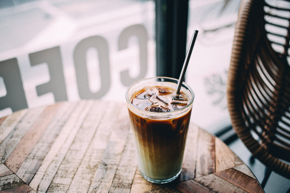 Café con hielo con pajita sobre una mesa junto a la ventana de una cafetería