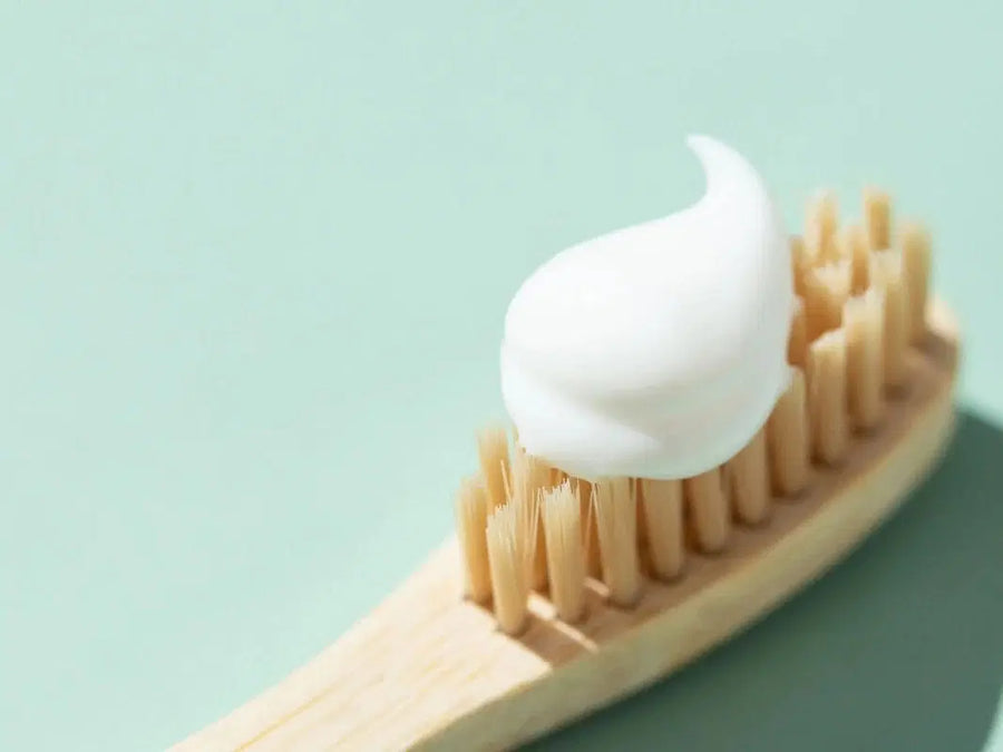 Cepillo de dientes de bambú con pasta dentífrica blanca sobre fondo verde