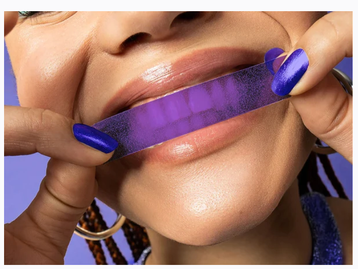 Mujer colocándose una tira blanqueadora morada sobre los dientes superiores