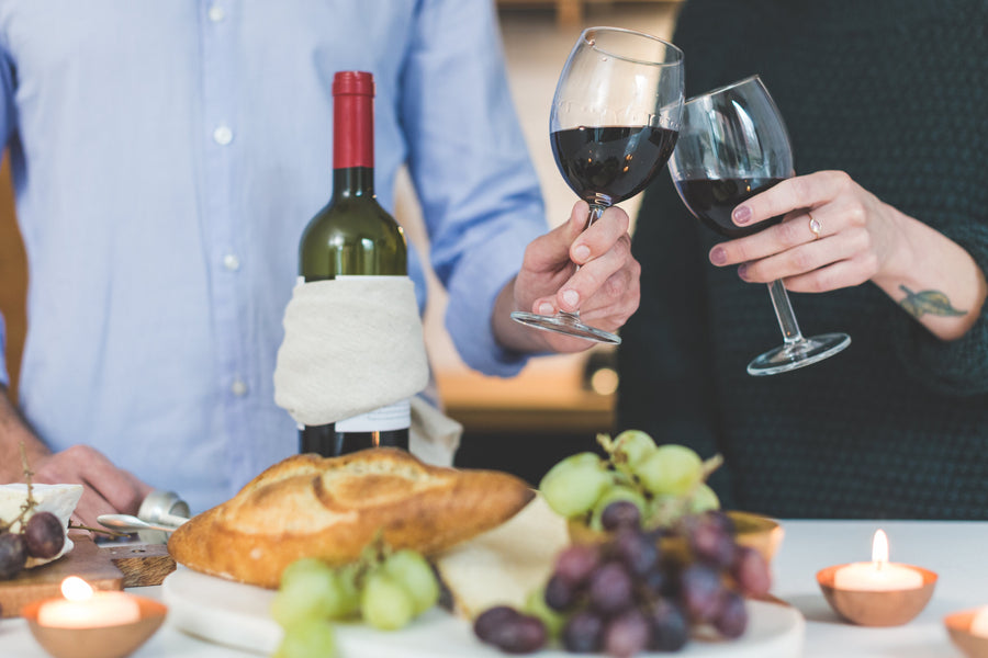 Dos personas brindando con copas de vino tinto en una mesa con pan y uvas